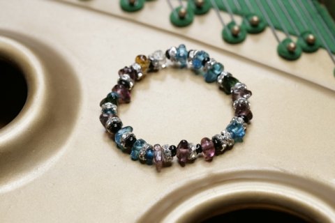 Brugbart armb�nd med mange farvede glasperler bl.a. bl�, gr�n ,sort, hvid, brunlig og hvid. Indeholder fors�lvet swarovski mellemled. Er lavet med elastik og m�ler ca.15 cm