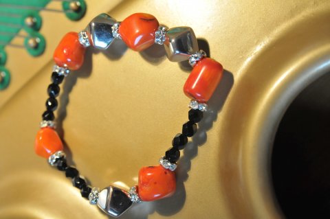 Orange koral armbnd med sorte facet sten. Indeholder ogs sm fine mellemled af forslvet rundel swarovski og balislv. Lavet med elastik og mler ca.19 cm.