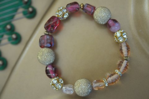 Forgyldt armbnd med rd/rosa nuancer. Flotte swarovski mellemled. Mler ca. 18 cm. Lavet med elastik.