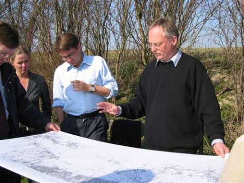 Brian Mikkelsen får en indføring i, hvad udgravningerne i 1990erne har frembragt af oldsager fortalt af Nydamselskabets formand, Vincent Jessen. Folketingsmedlem i Sønderborgkredsen Ellen Trane Nørby (V) ser interesseret med. Medarrangør af besøget, Formand for De Konservative i Sønderborg, John Lohff, skimtes.
