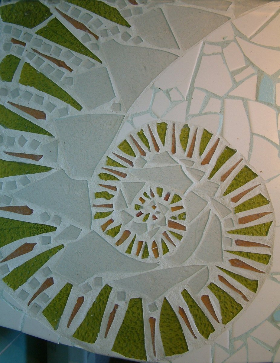 Mosaik med spiralform i grønt, gyldent og transparent glas af Lotte Rosenkilde